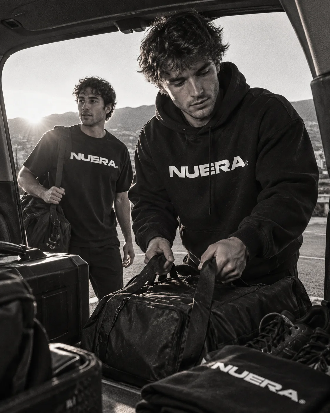 Two people loading duffel bags into a car in NUERA hoodies and tees.